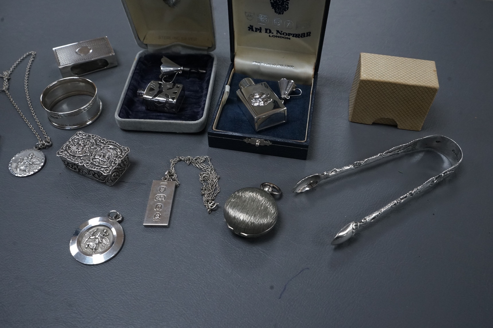 A group of mainly modern silver collectables including three assorted scent flasks and funnels by Ari D. Norman, two money clips, matchbox sleeve, napkin ring, pill box, three pendants including ingot and a pair of Victo